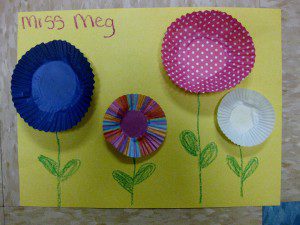 A photo of colorful cupcake liners glued to a yellow piece of paper with green stems and leaves drawn beneath them.