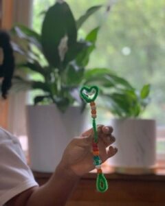 A photograph of a pipe cleaner with beads on it shaped into a wand with a heart outline on top.